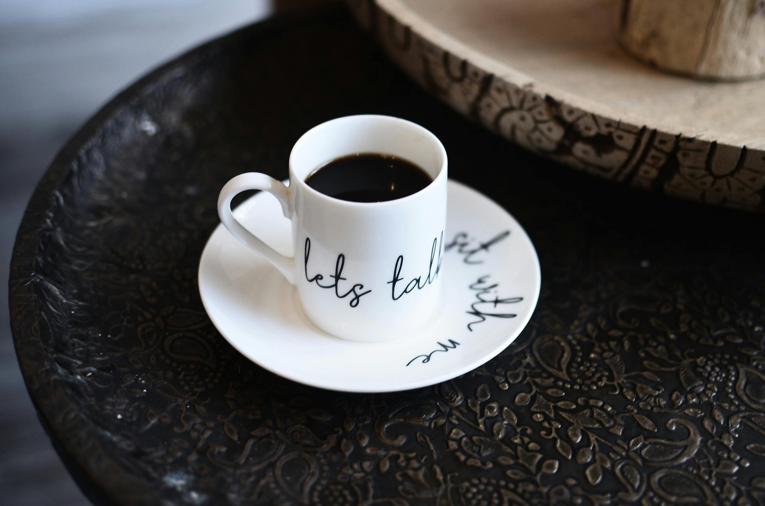 Close-up of a ceramic mug filled with black coffee, set on an intricately designed table indoors.